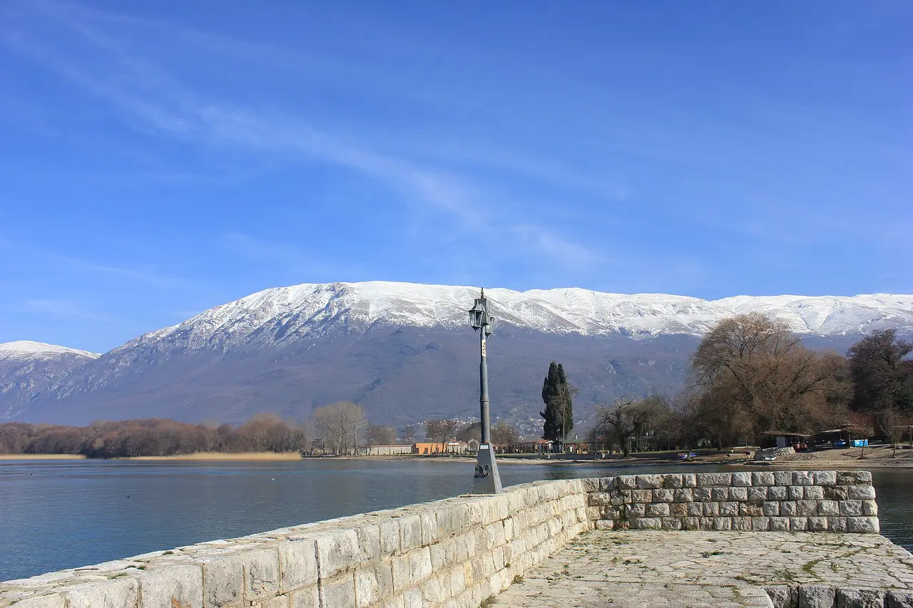 Lake Ohrid from a stone jetty with an old lamppost and the snow-capped Galicica mountains behind