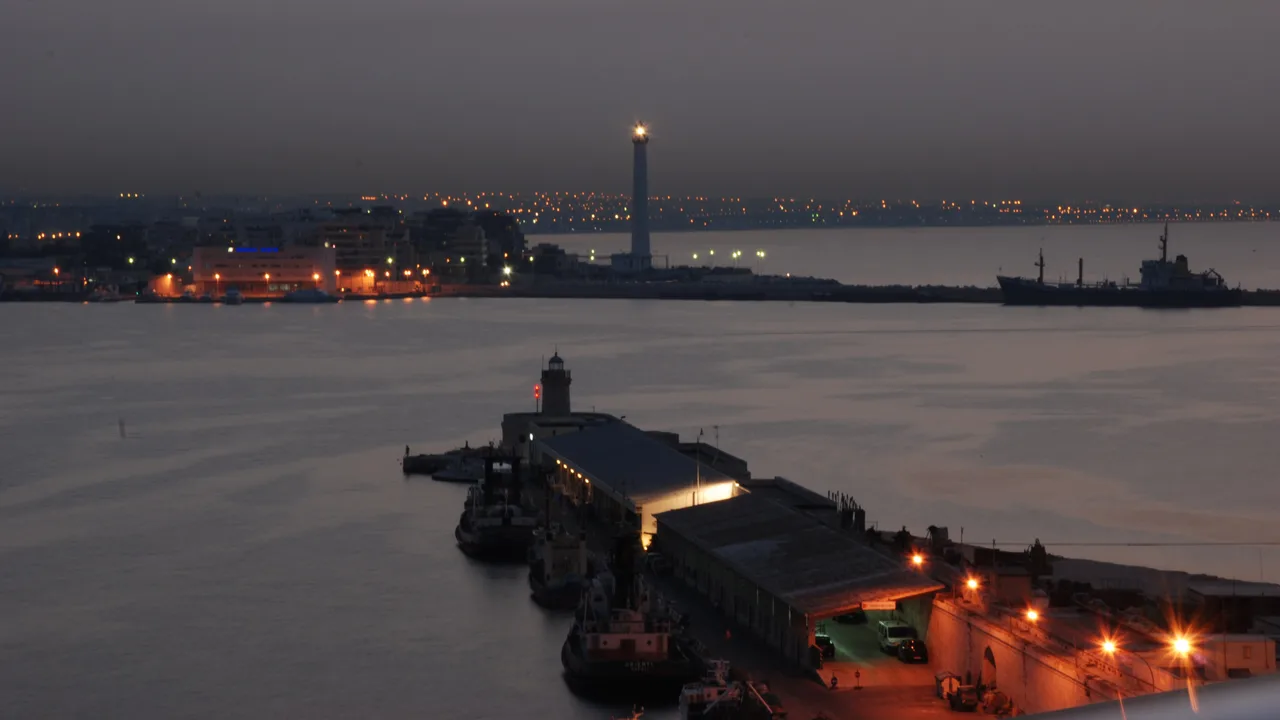 The port of Bari at dusk with the harbour lighthouse, quays and the city lights along the Adriatic behind