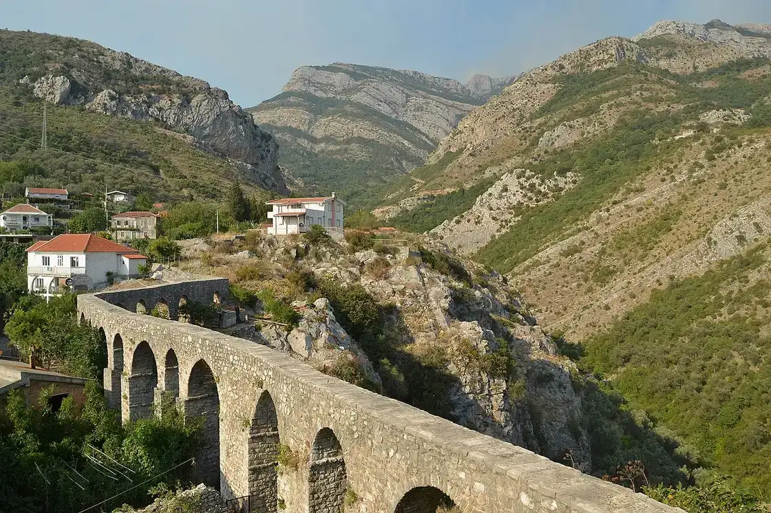 The stone arches of the old Bar aqueduct crossing a green valley below the mountains