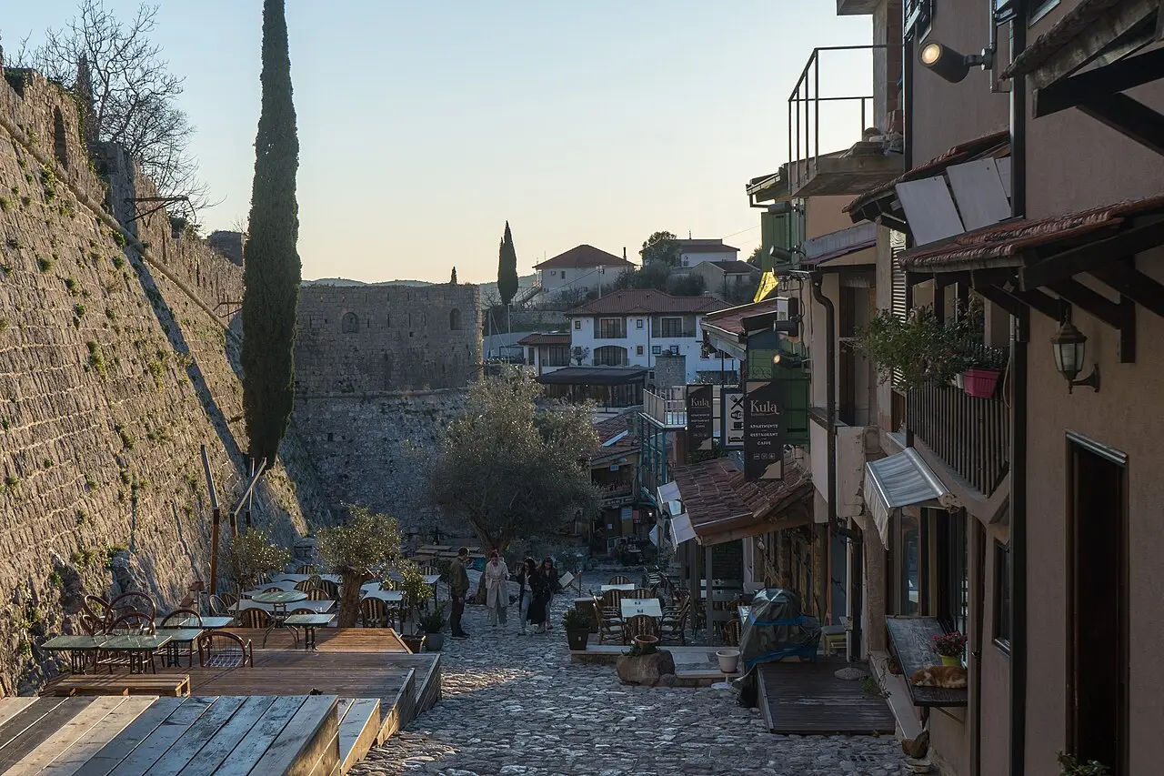 The high stone fortress wall of Stari Bar above a cobbled café-lined lane at dusk