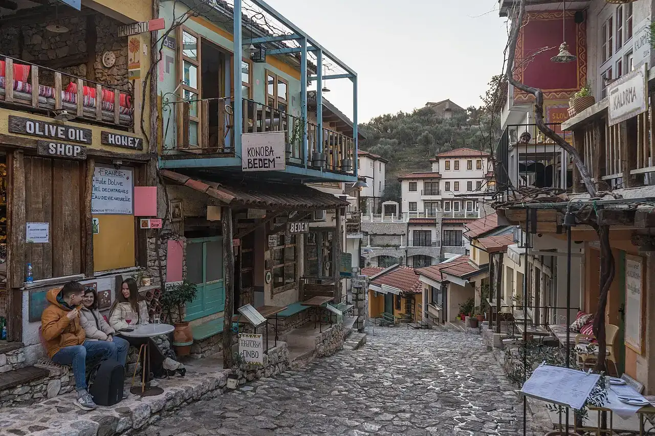 A cobbled lane in Stari Bar lined with an olive oil shop and konoba, with the ruined town behind
