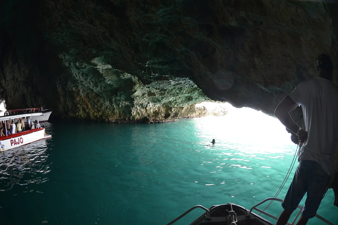 Mouth of the Blue Cave on the Luštica peninsula with a tour boat at the entrance and a swimmer in the lit water, photographed in 2019