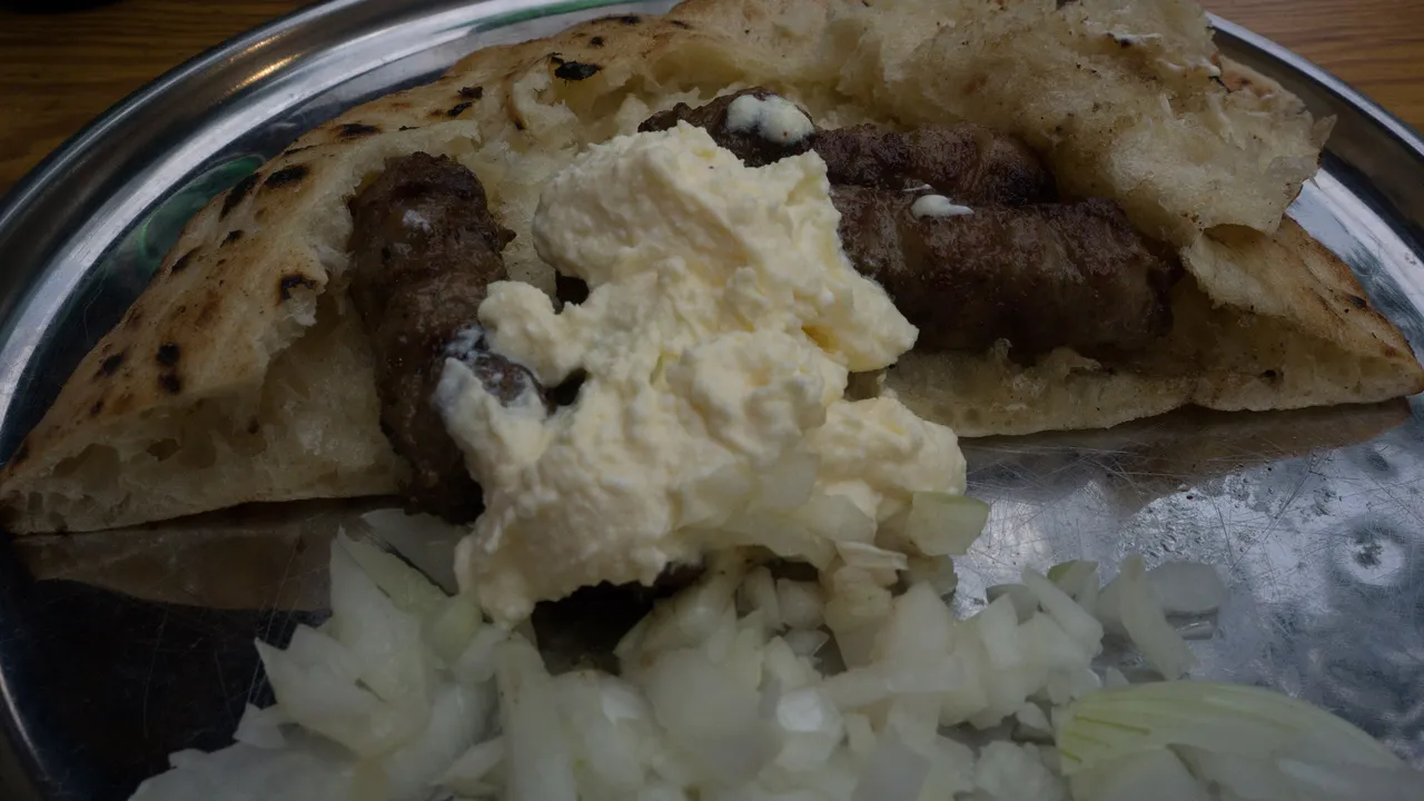 Cevapi tucked into flatbread with kajmak and chopped onion on a metal tray