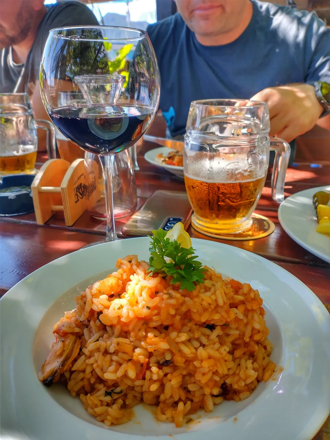 A plate of seafood risotto with mussels and prawns, a glass of red wine and a beer on a restaurant table