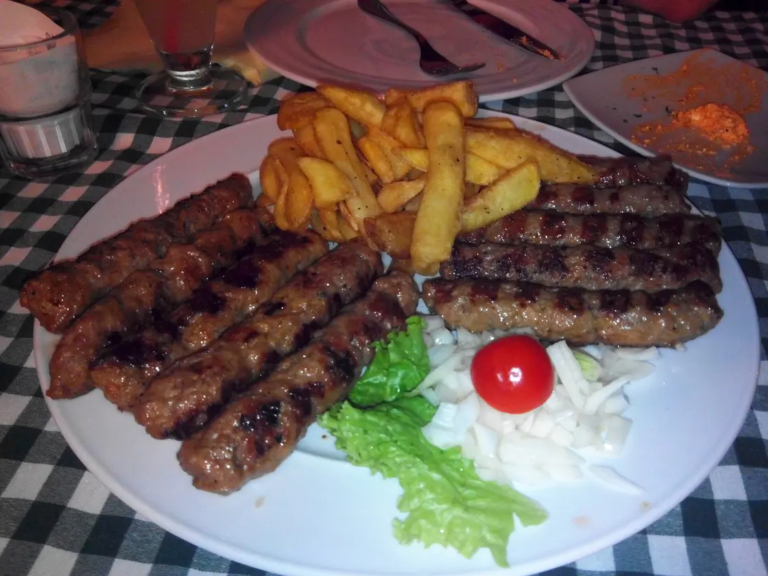 Plate of grilled ćevapi sausages with onion, bread and salad