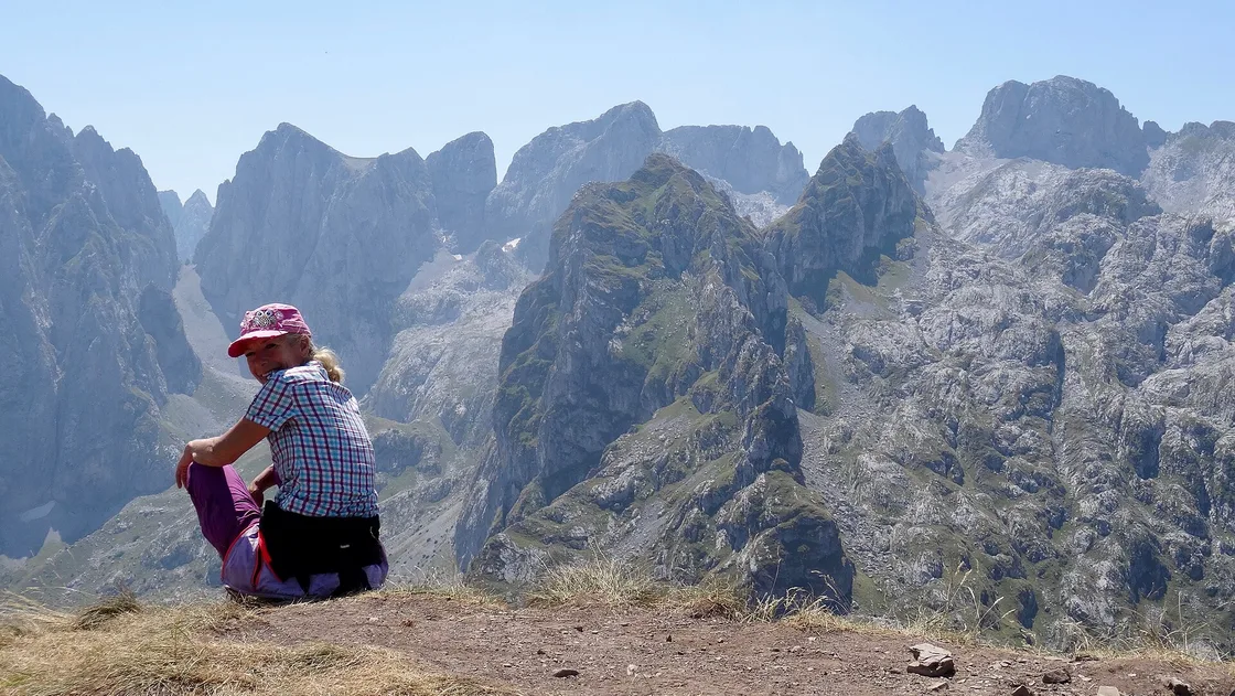 A hiker resting on a grassy ridge with the jagged Karanfili peaks of Prokletije behind, Montenegro