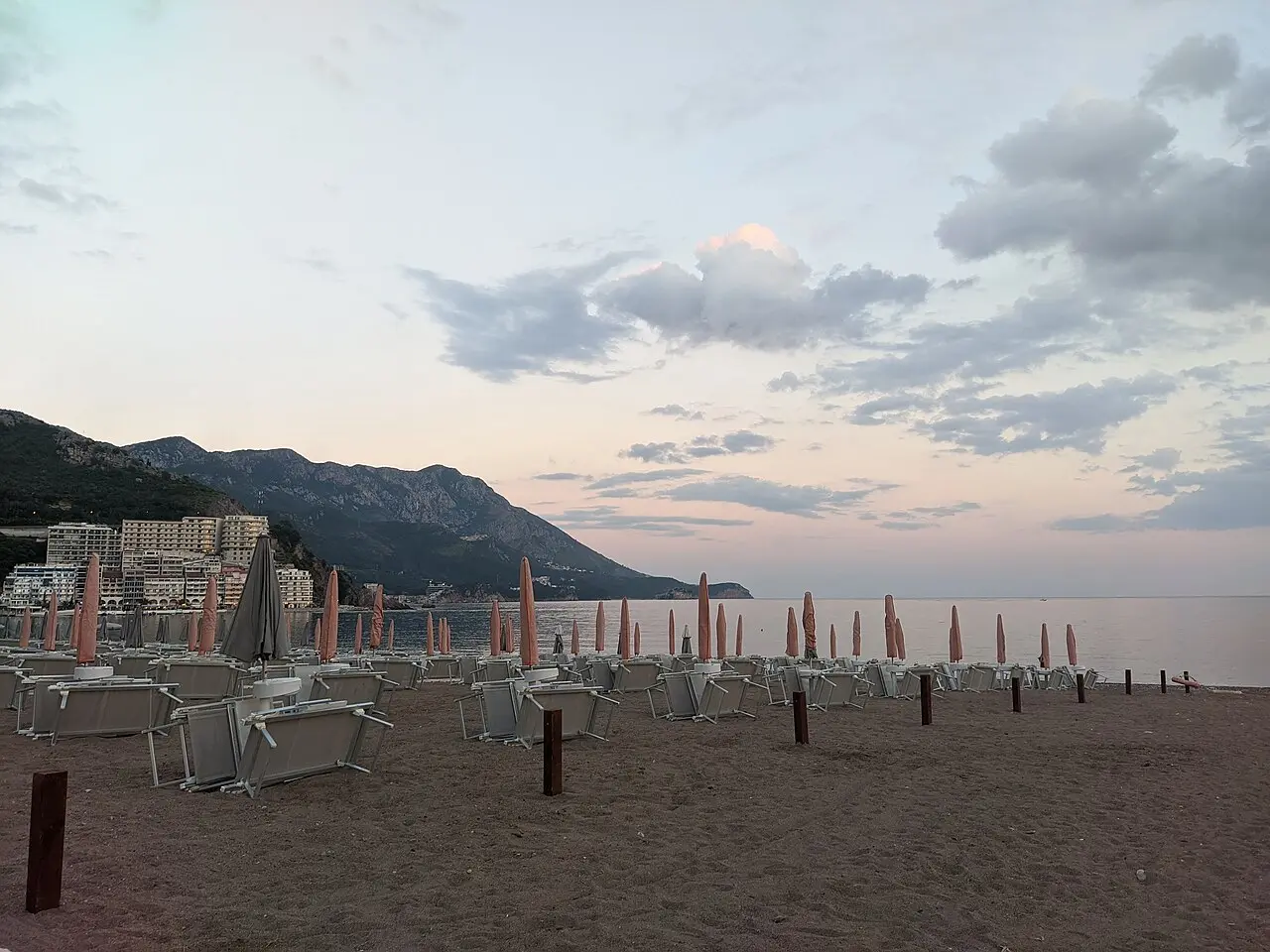 Bečići beach near Budva at dusk, loungers and folded umbrellas on the sand with the riviera hills behind