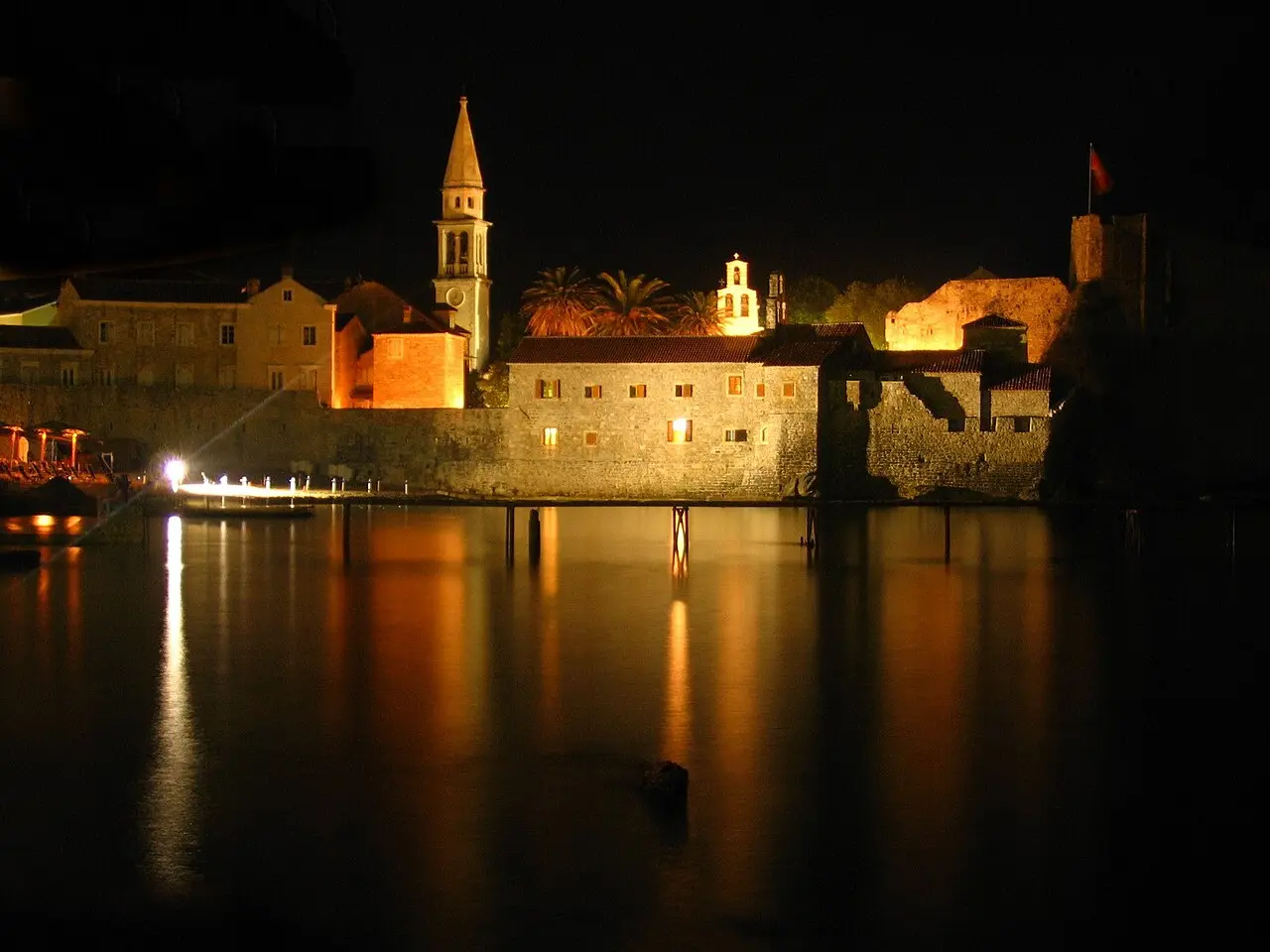 Budva Old Town walls, bell tower and citadel lit up gold at night above the water