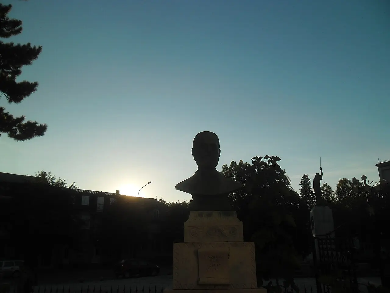 A bronze bust silhouetted against the sunset on a square in Cetinje at dusk