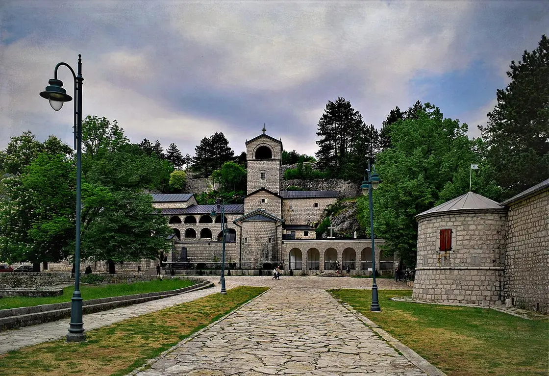 The Cetinje Monastery seen from the approach path, with its round tower, bell tower and a lamppost under a moody sky