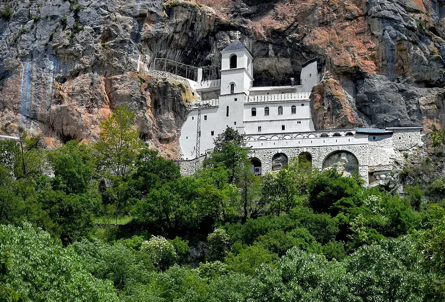 Ostrog Monastery, a white church built into a vertical grey cliff above green woods