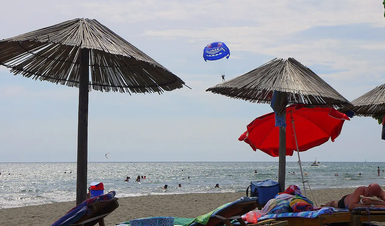 Straw parasols and sunbeds on the long sandy beach at Ulcinj with a parasailer over the sea