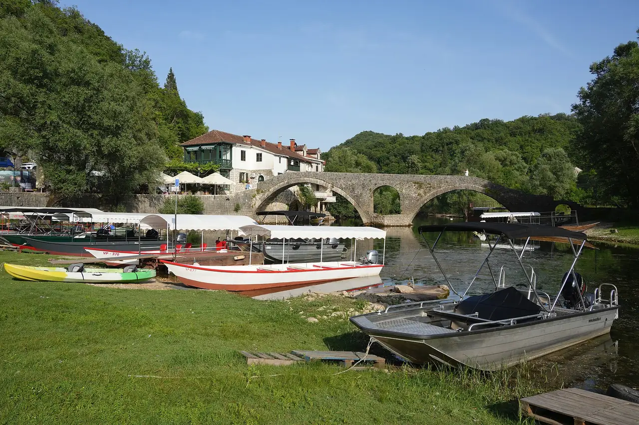 Danilo two-arch stone bridge at Rijeka Crnojevica, boats in the grass and tiled houses behind
