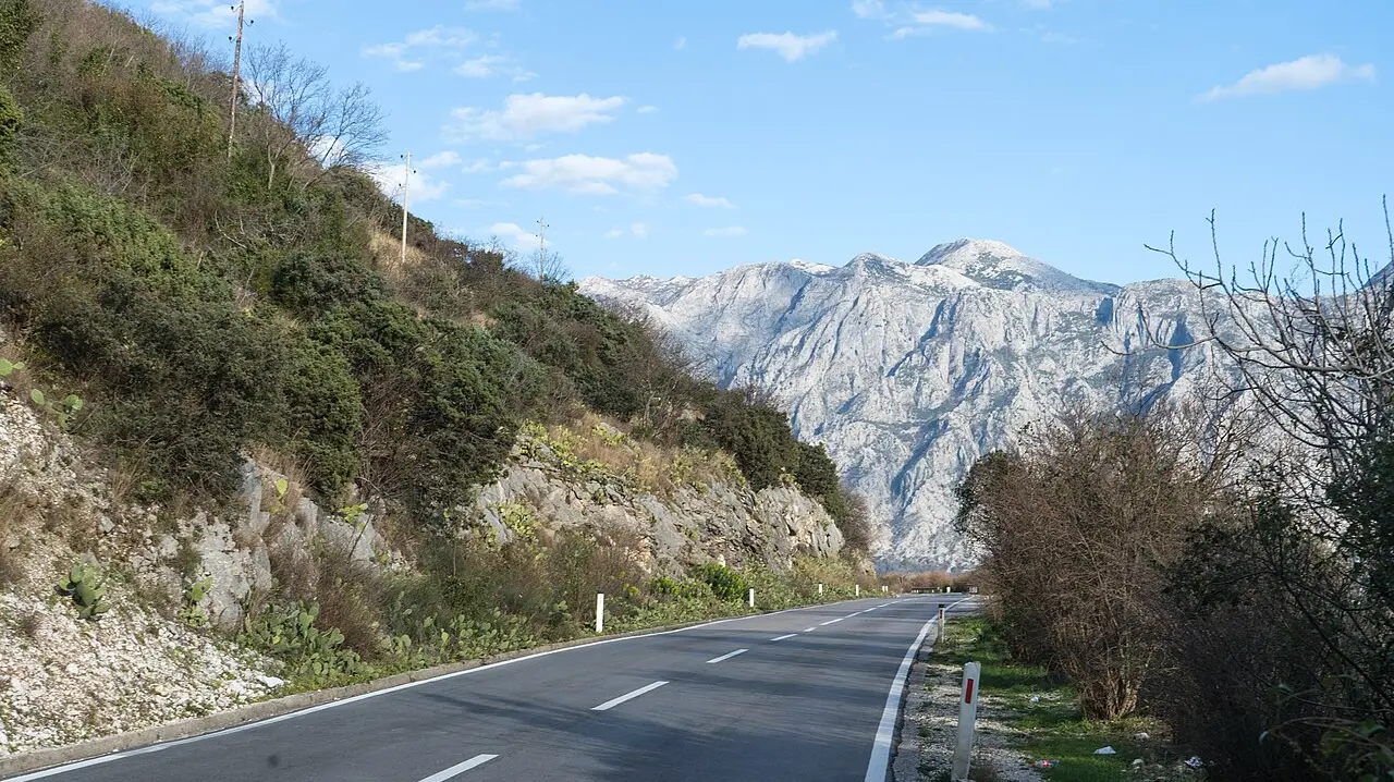 Narrow two-lane coastal road hugging the shore between Perast and Dobrota on the Bay of Kotor, Montenegro