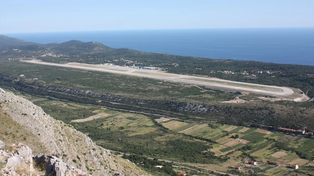 Dubrovnik Airport seen from the hills above Konavle: the runway, terminal and control tower on the coast, with the Adriatic behind