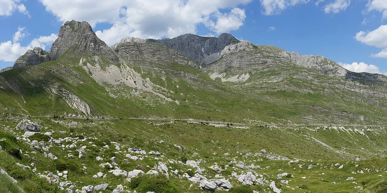 The Durmitor Ring road cutting across a green karst mountainside near the Sedlo pass, jagged peaks behind