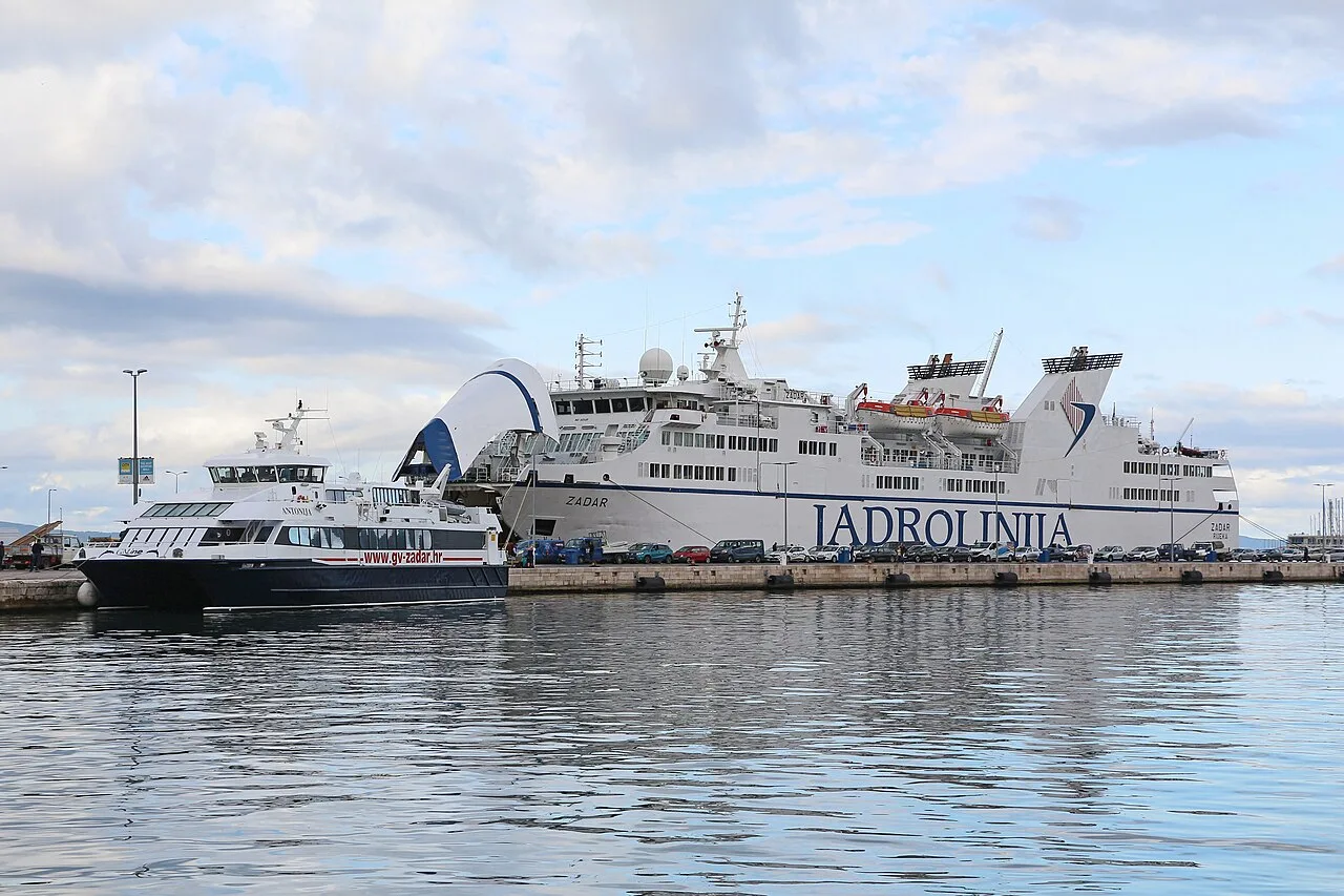 A Jadrolinija ro-pax ferry berthed with cars lined up on the quay ready to load