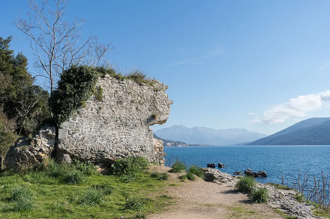 The ruined stone wall of the old Venetian citadel of Herceg Novi on the shore with the bay behind