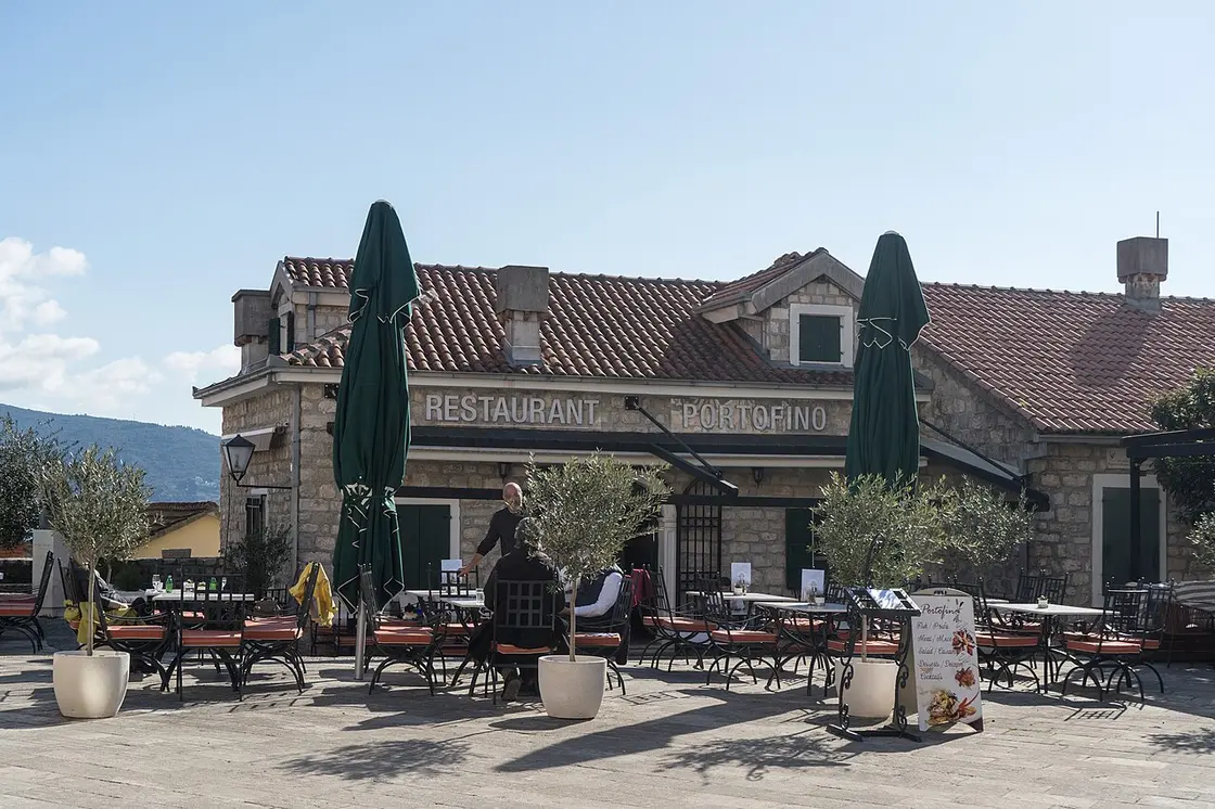 A café terrace with green umbrellas and potted olive trees on a square in Herceg Novi Old Town