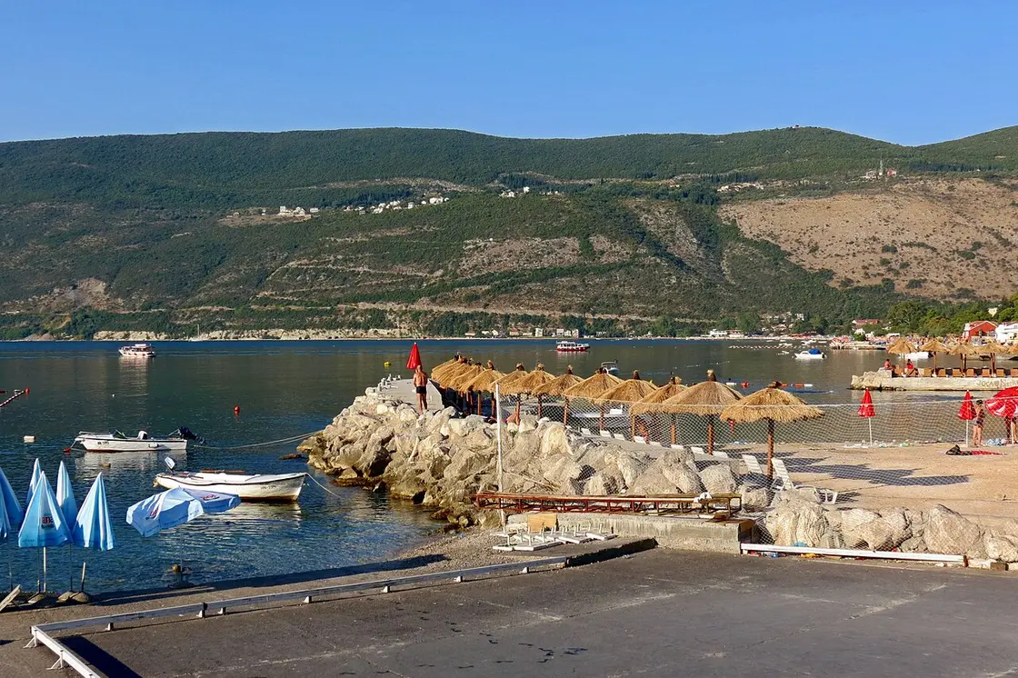 A pebble beach with thatched umbrellas and small boats on the Herceg Novi riviera