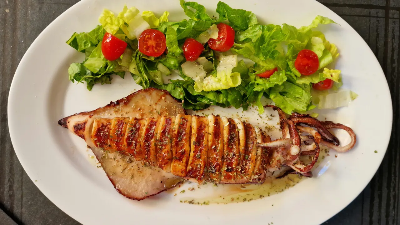 Grilled squid with a fresh salad on an oval plate