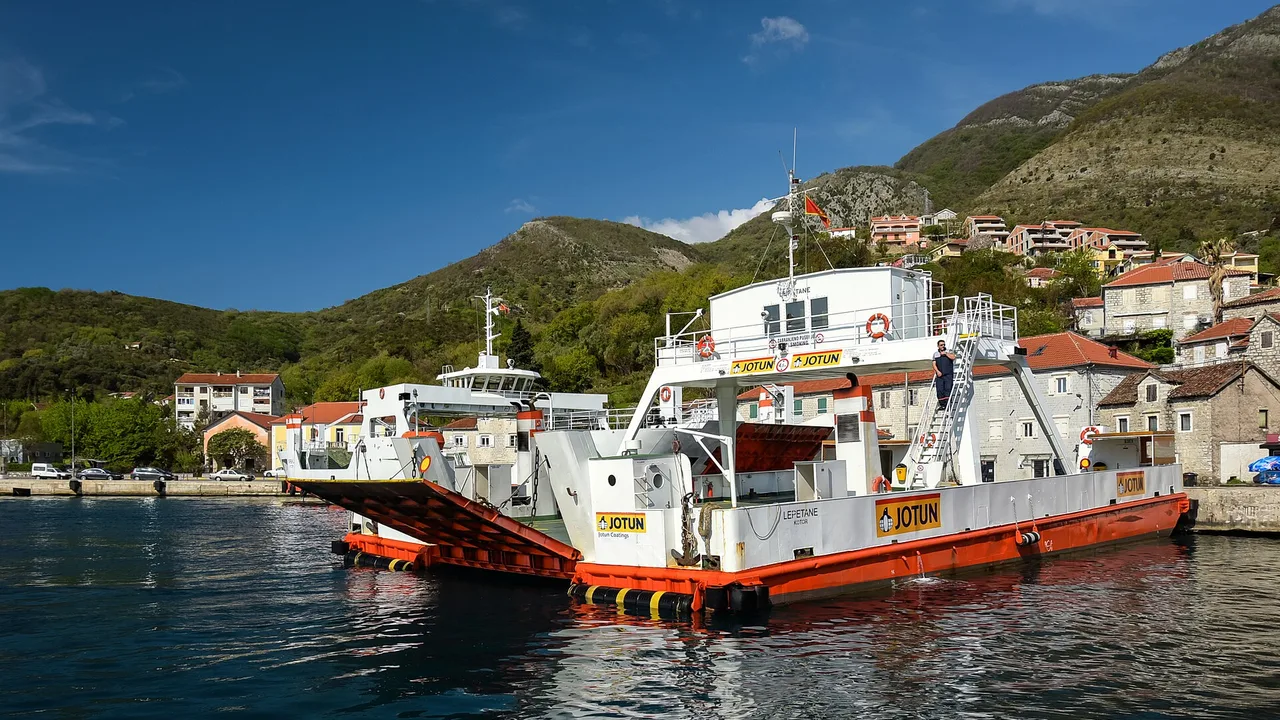 Two Kamenari-Lepetane car ferries moored at the Lepetane ramp on the Bay of Kotor with the village and hills behind