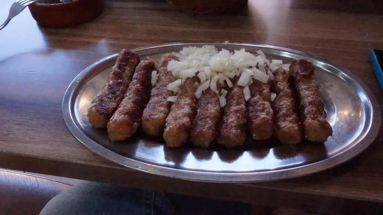 Platter of grilled cevapi with chopped onion on a metal tray