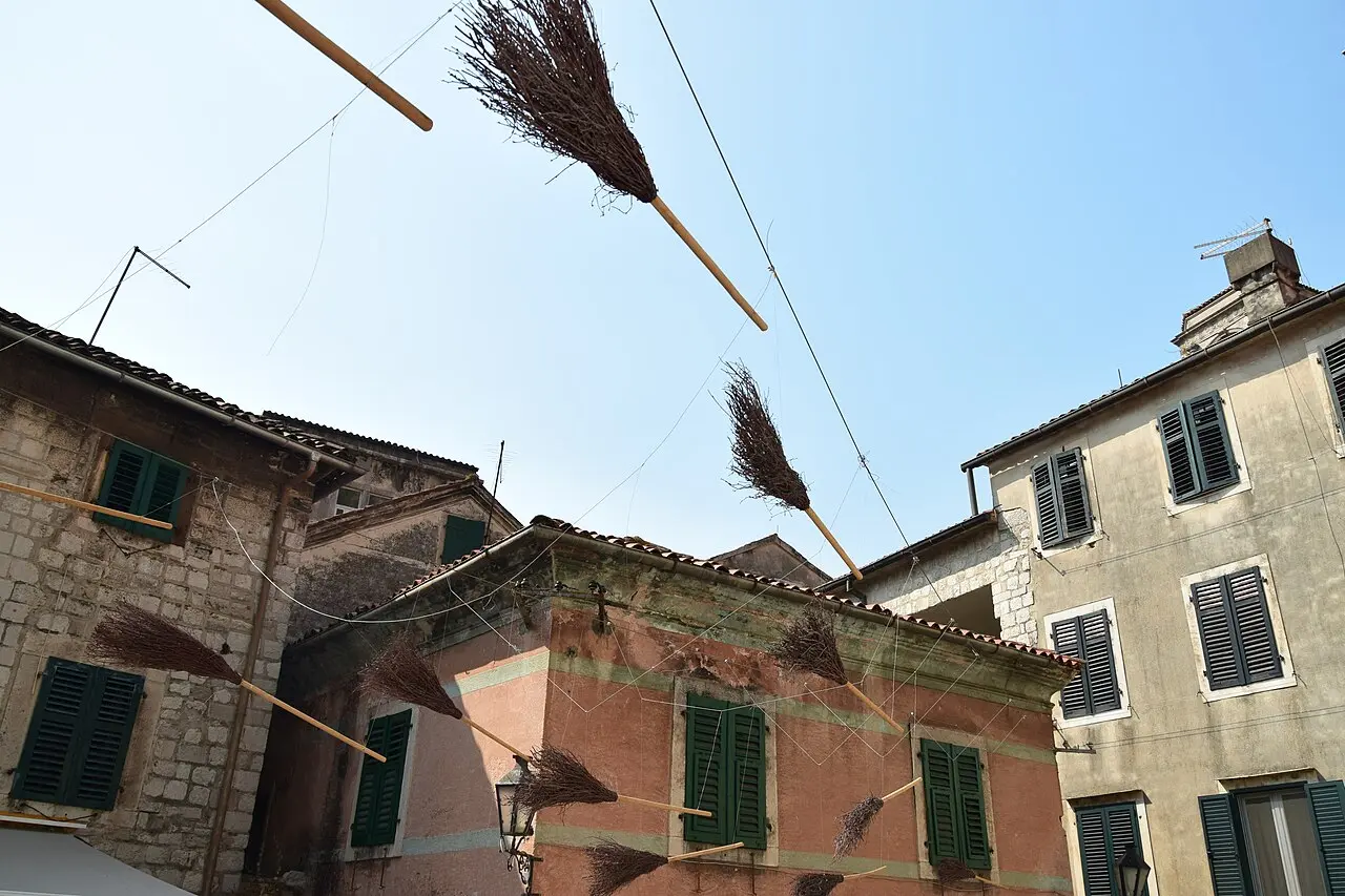 Laundry and brooms hanging over a narrow stone lane in Kotor Old Town below old houses