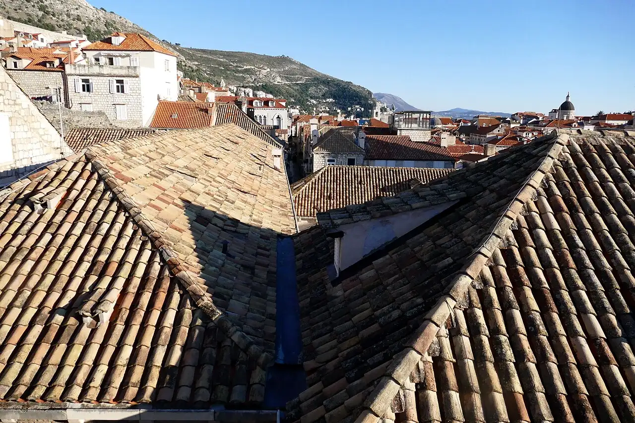 Terracotta rooftops of Dubrovnik old town seen from the city walls, with a church dome and hills behind
