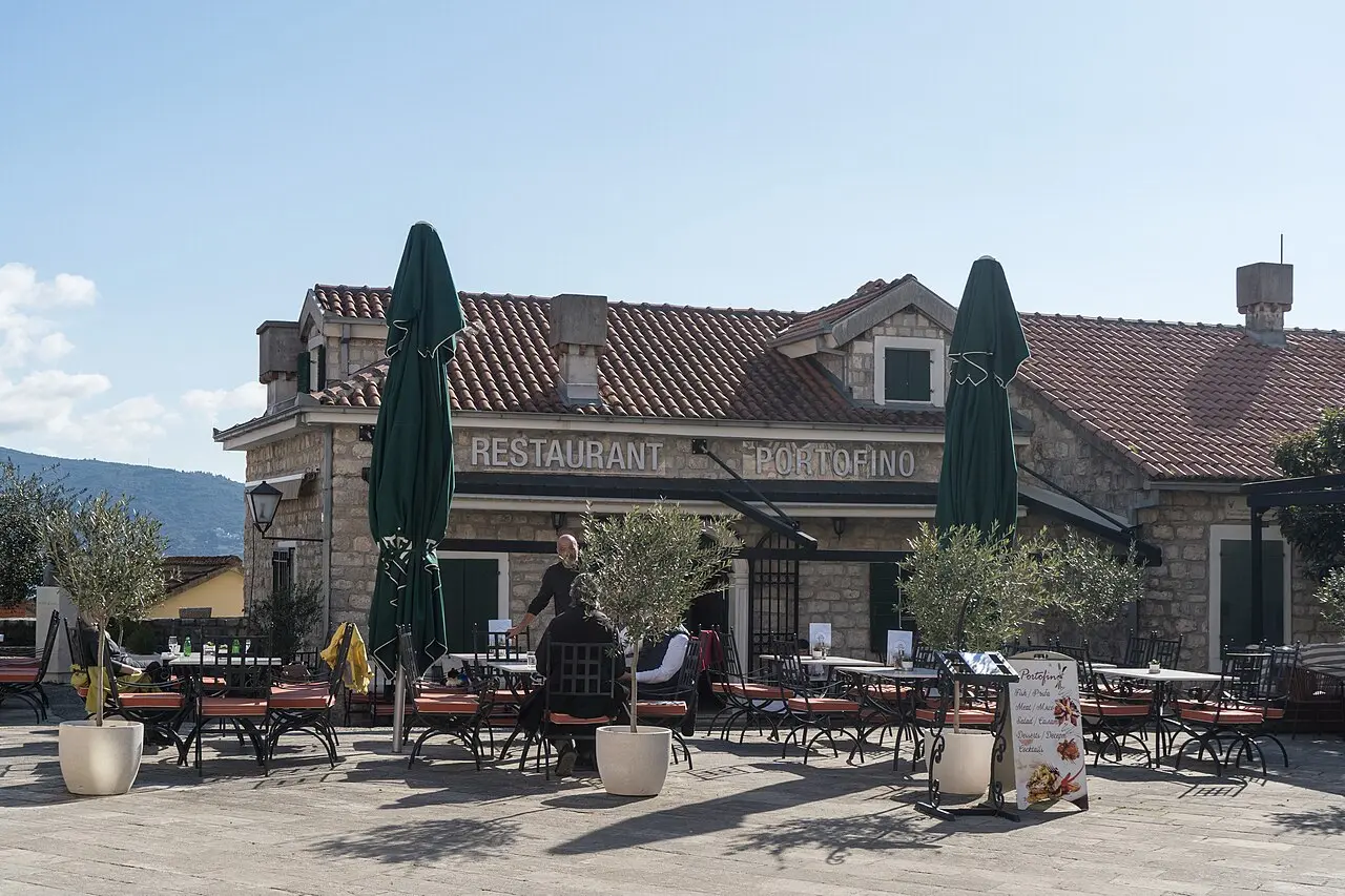 Cafe tables and umbrellas under olive trees on a stone square in Herceg Novi old town