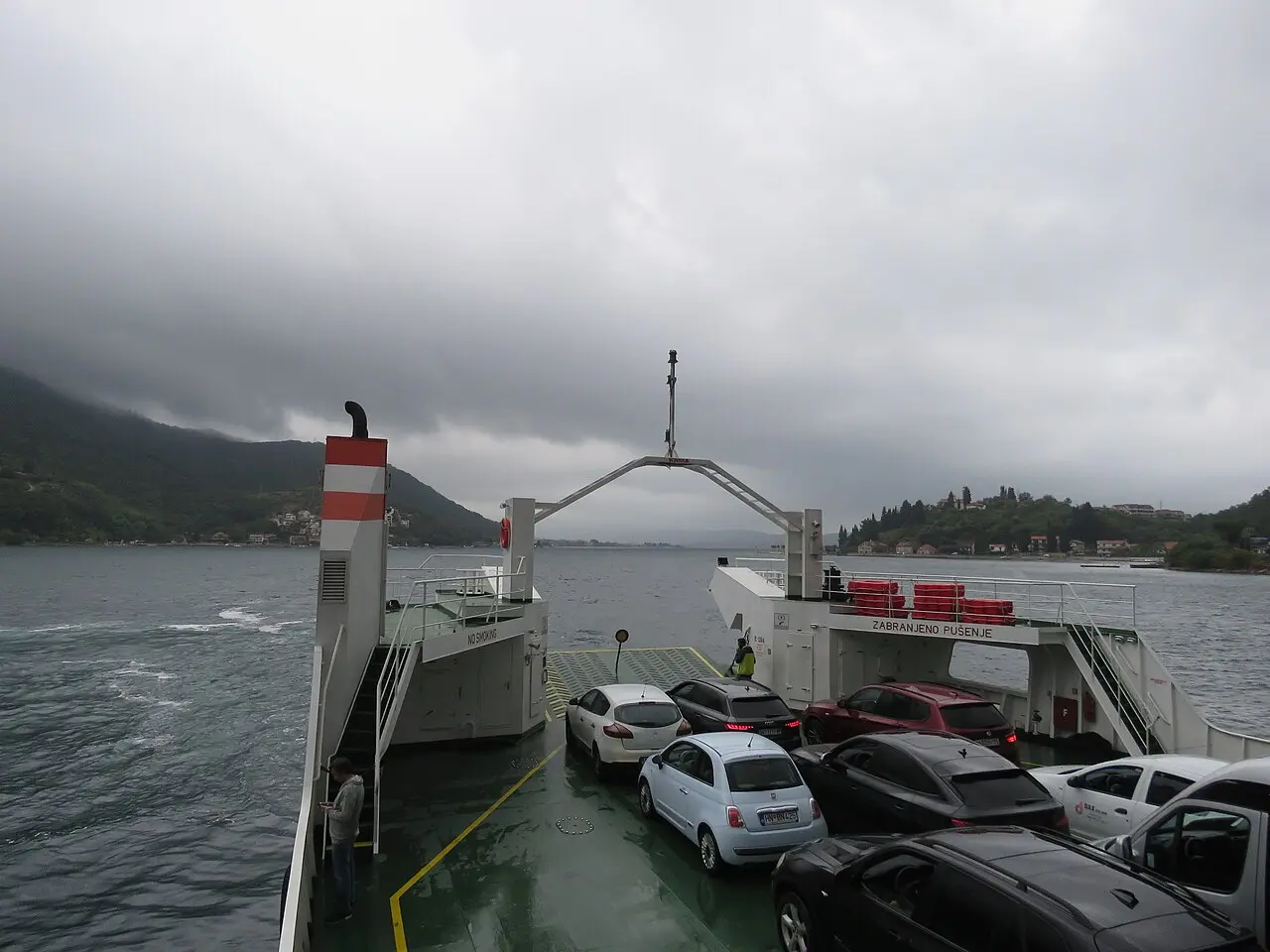 Cars on the deck of the Kamenari-Lepetane ferry mid-crossing on the Bay of Kotor under a grey sky