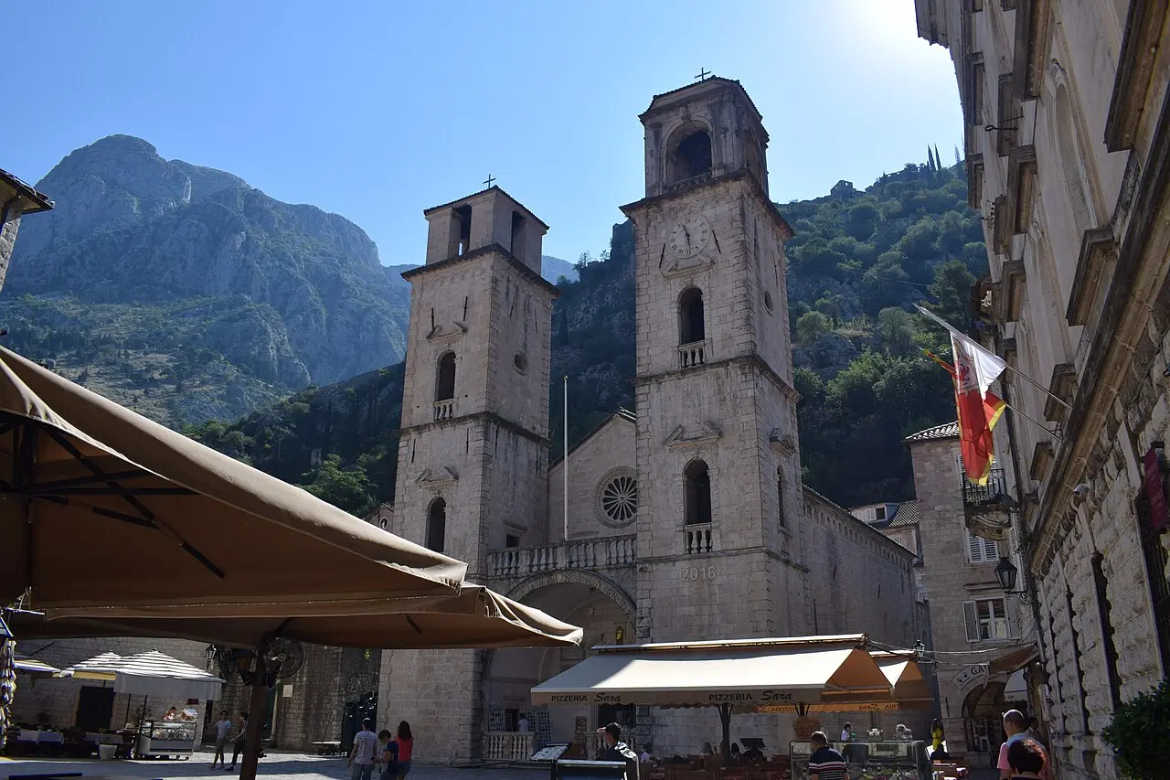 The two asymmetric bell towers of Saint Tryphon Cathedral seen from the café-lined square in Kotor