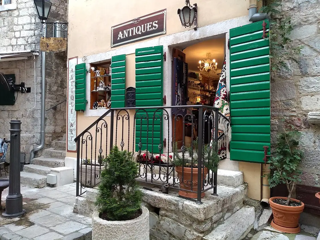 A narrow stone lane in Kotor Old Town with a green-shuttered antiques shop