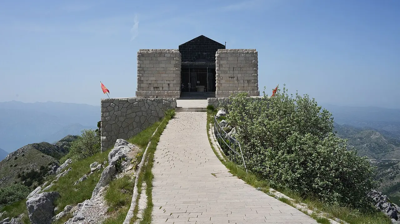 The stone Njegoš Mausoleum on the Jezerski vrh peak of Lovćen, Montenegro, with a paved path and the Montenegrin flag