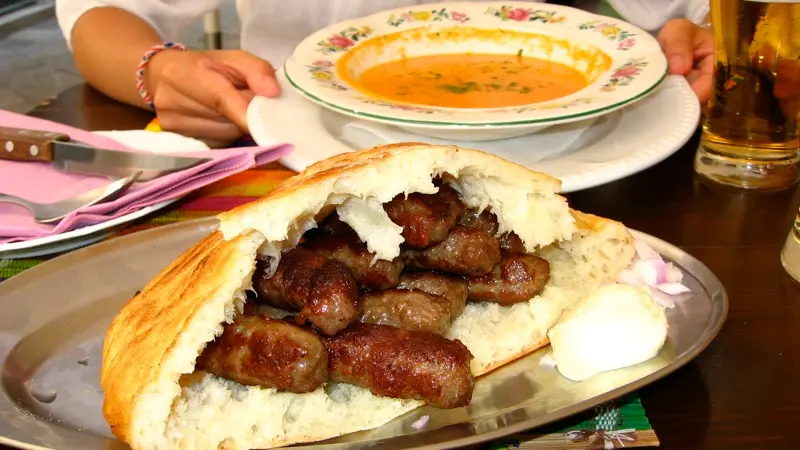 Grilled ćevapi served in flatbread with kajmak and chopped onion on a metal plate