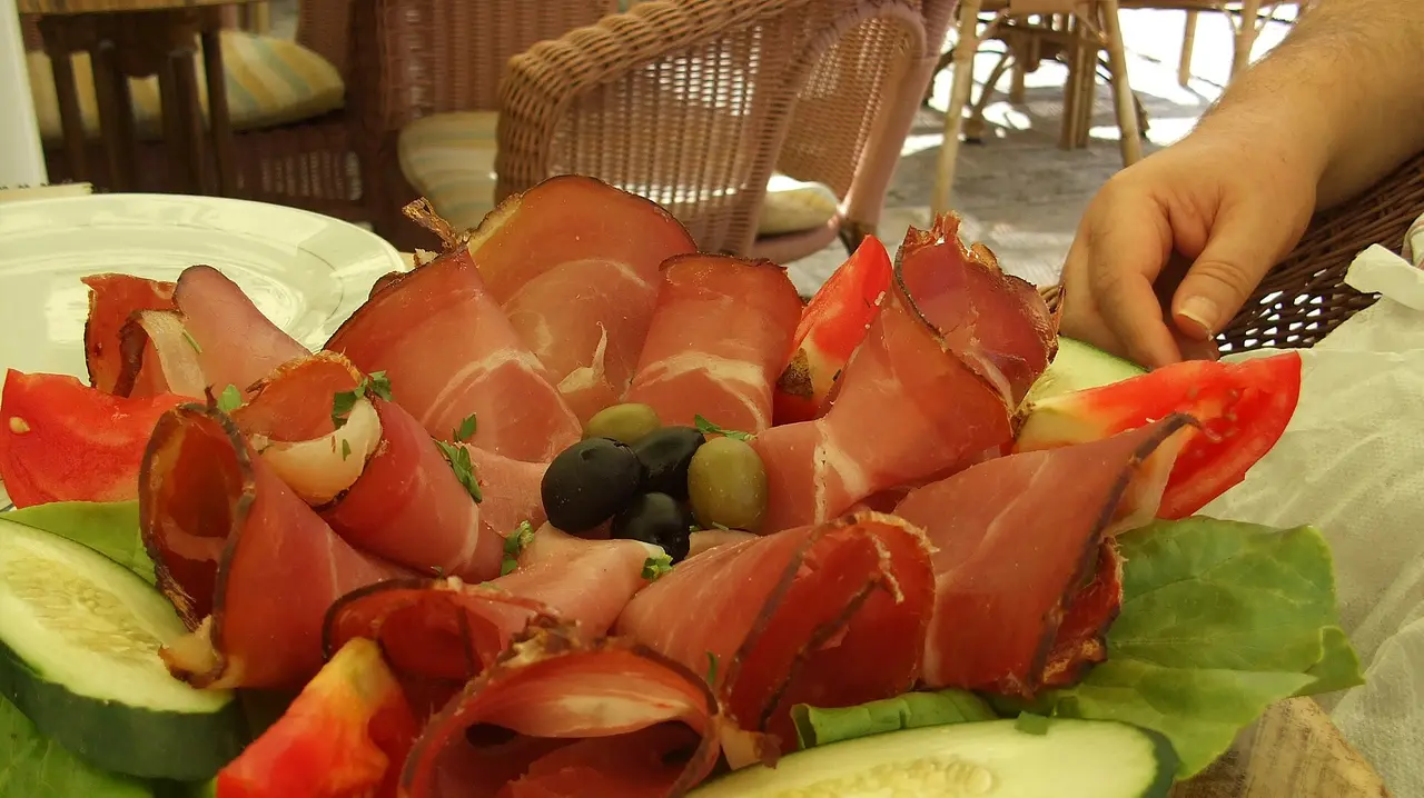 A platter of thinly sliced Njeguški pršut with olives, tomato and cucumber on a terrace in Budva, Montenegro