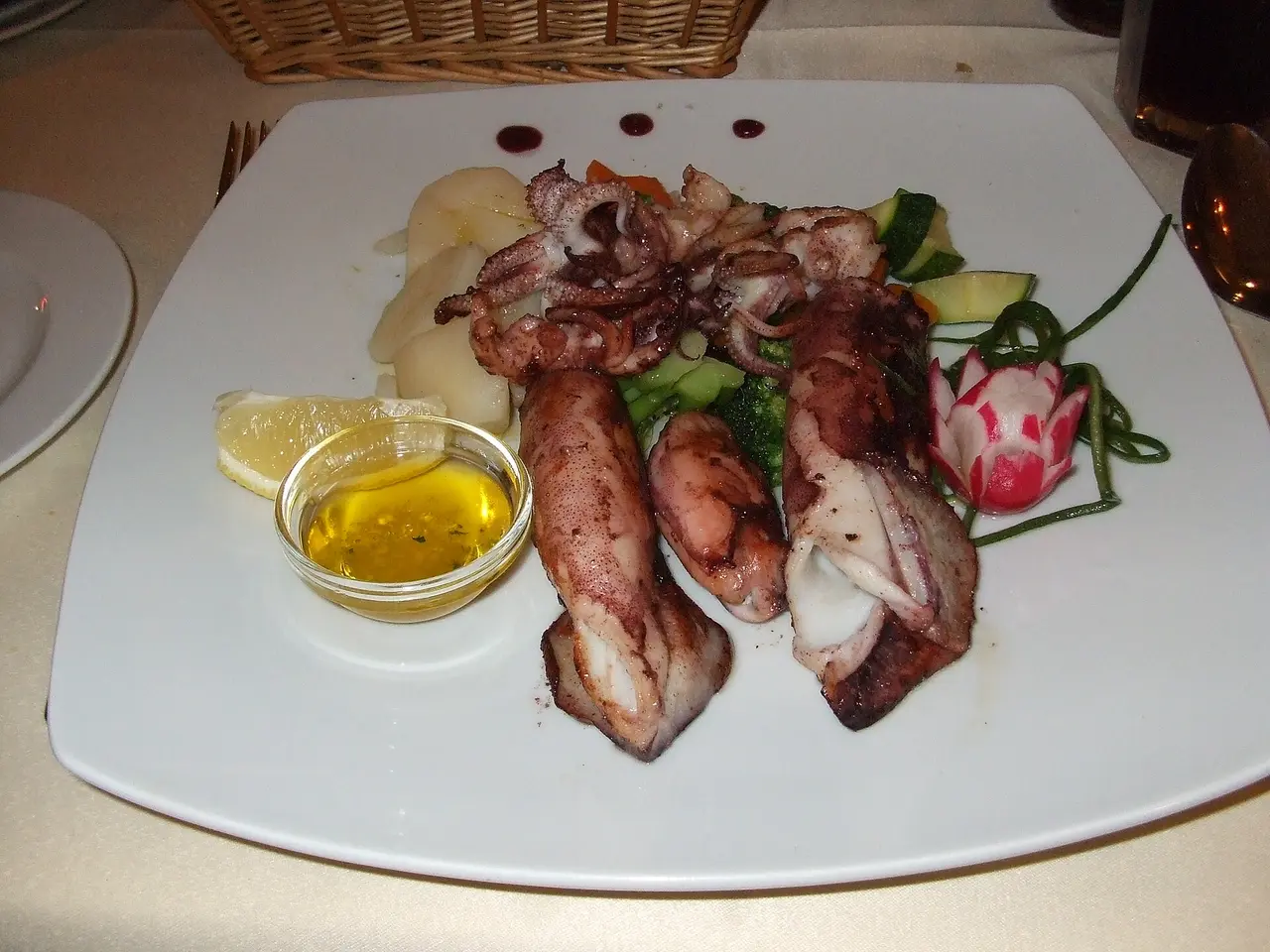 A plate of grilled squid with vegetables and a bowl of olive oil dressing at a coastal konoba