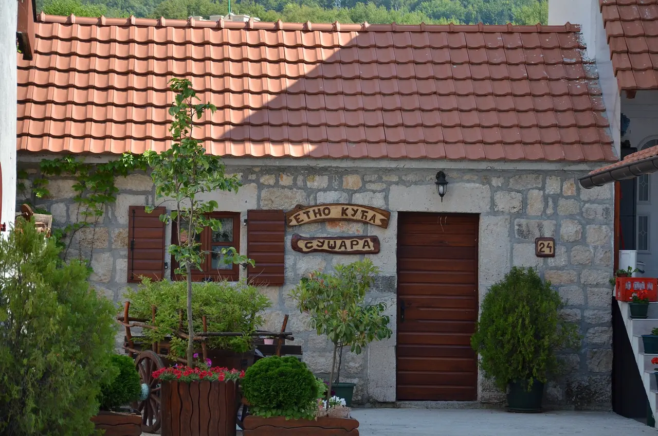 A stone village house in Njeguši with a wooden sign reading Etno kuća - Sušara, the drying house where ham is cured, Montenegro
