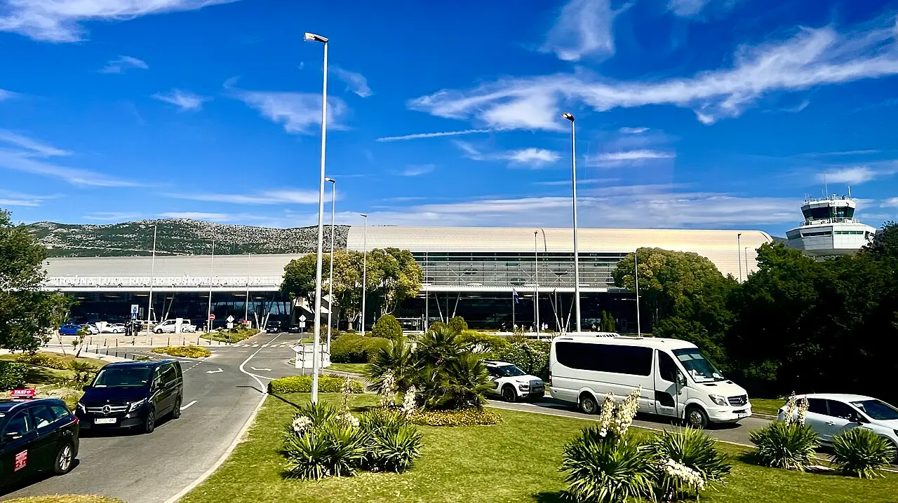 A white transfer minibus and cars outside the terminal at Dubrovnik Airport