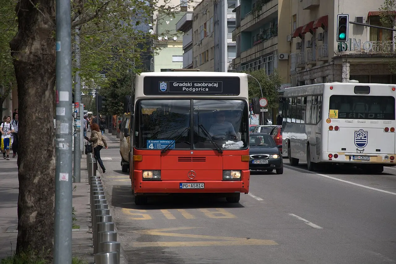A red city bus on a street in Podgorica with another bus behind it