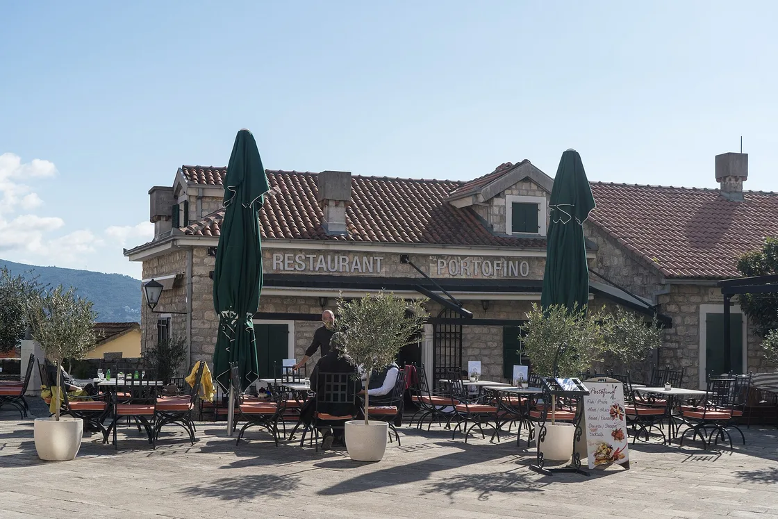 Tables and green umbrellas outside a restaurant on a stone square in Herceg Novi Old Town