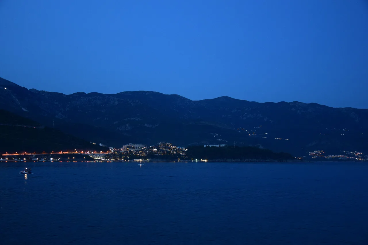 Budva waterfront and marina lit up on a summer night with the old town and hills behind