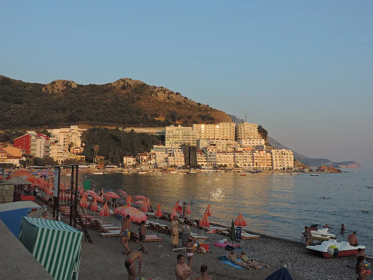 Sun-loungers and swimmers on a Budva Riviera beach at golden hour, Montenegro