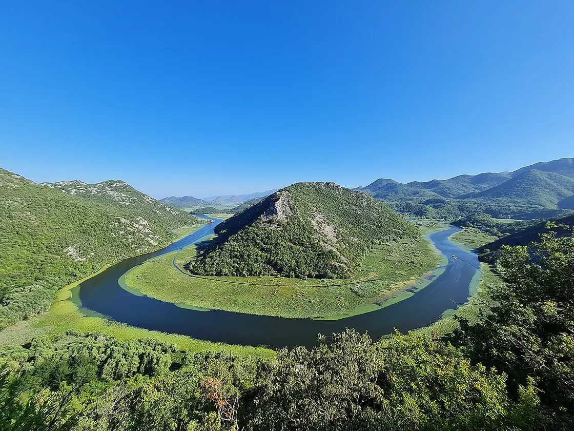 Wide summer view of the green horseshoe river bend of Rijeka Crnojevića at Lake Skadar, a boat on the water