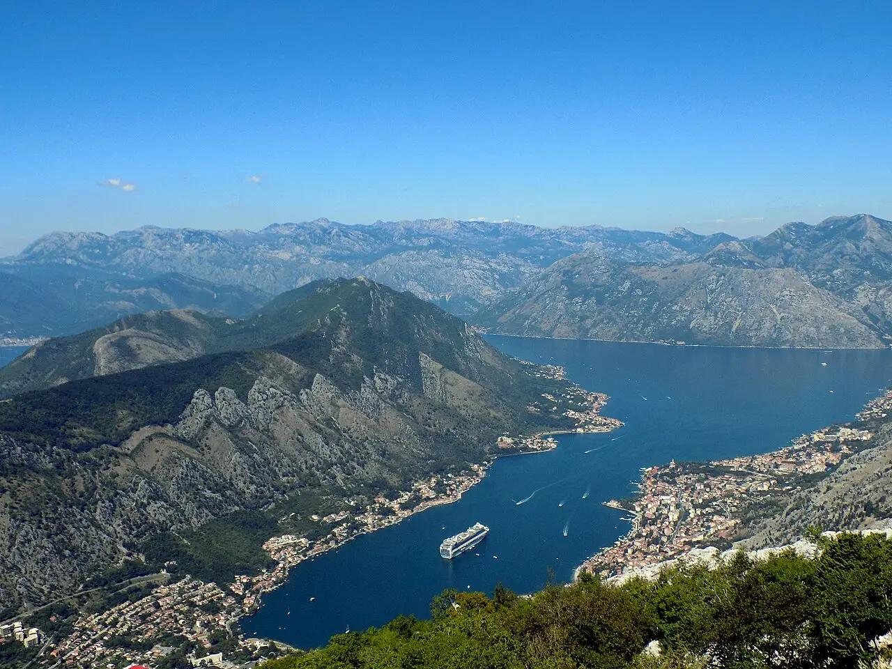 Aerial view of the Bay of Kotor with a cruise ship docked below Kotor's old town, seen from the mountain road above