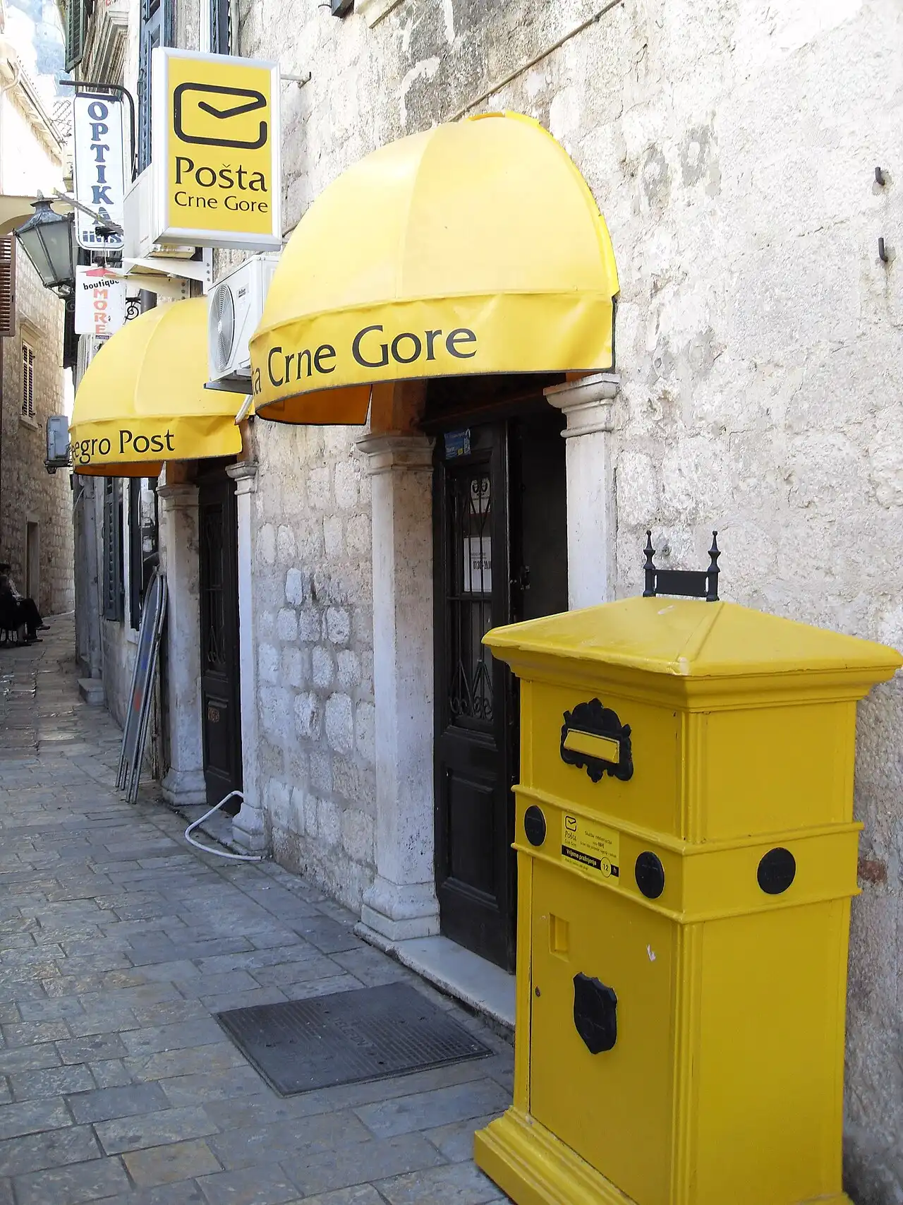 Yellow-awninged Montenegro Post office and post box on a stone-paved street in Kotor's old town