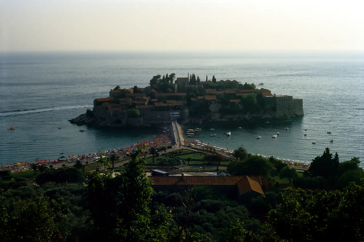 The fortified islet of Sveti Stefan in Montenegro, red-roofed stone houses on a rock joined to the shore by a narrow isthmus