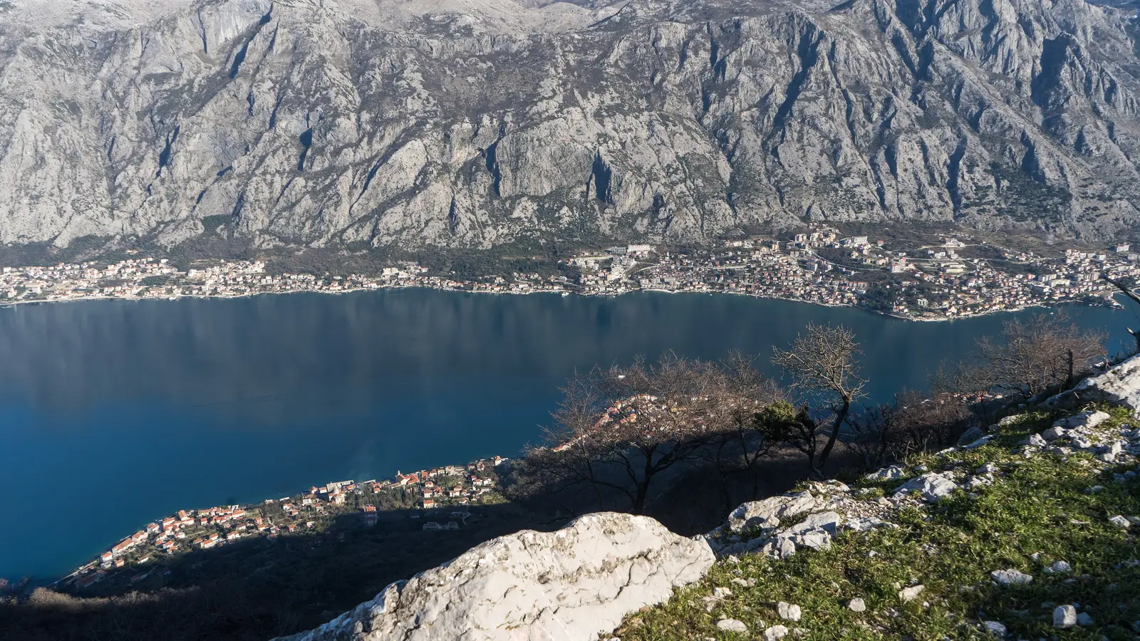 View over the Bay of Kotor from Vrmac mountain, blue water below and grey peaks behind the coast
