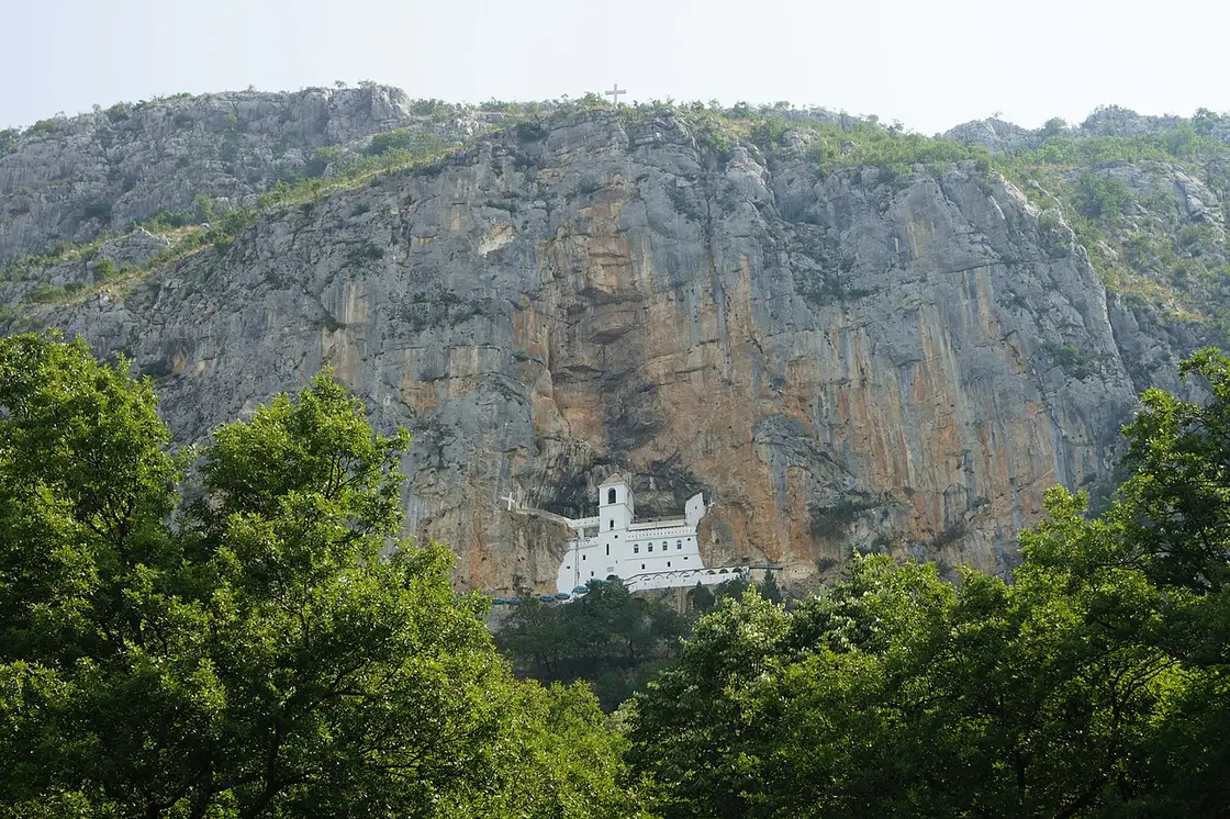 Ostrog Monastery's white Upper Monastery set into a sheer grey cliff above green forest