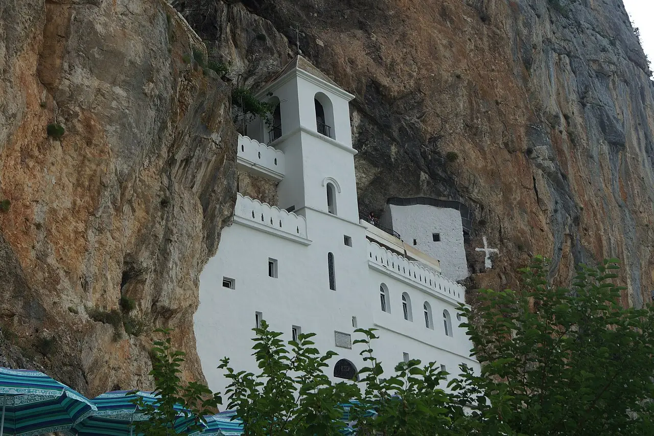 Ostrog Monastery as a white block in a sheer grey cliff, forest on the slopes below